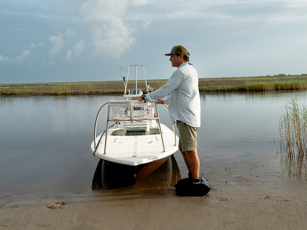 Angler with fishing apparel, boat, and mudder boots with a very scenic background view