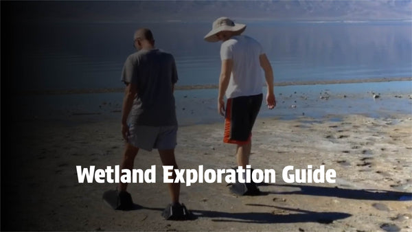 Two explorers walking across a vast wetland area wearing Mudder Boots.